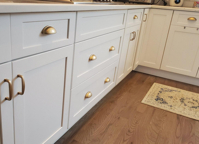 White kitchen cabinets with the 1399 cup pulls by Cosmas hardware in the gold champagne finish. The kitchen has hardwood floors and deep golden cabinet pulls and cup pulls. 