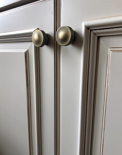 Brushed antique brass cabinet knobs, round on two taupe colored cabinets. 