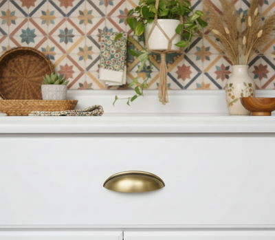 White cabinet with brushed antique brass cup cabinet handle against a decorative tiled wall.