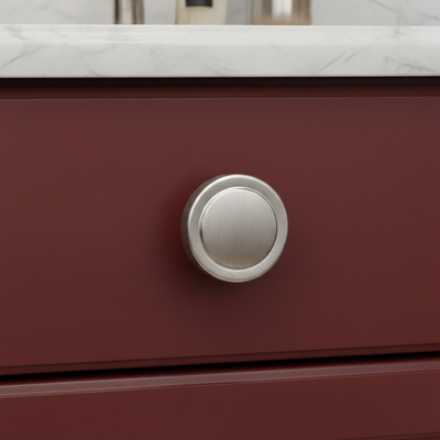 Close-up of a red drawer with a satin nickel handle on a white marble countertop.