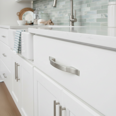 Close-up of white kitchen cabinets with satin nickel handles and a tiled backsplash.