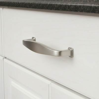 Close-up of a silver cabinet handle on a white cabinet with a dark countertop.