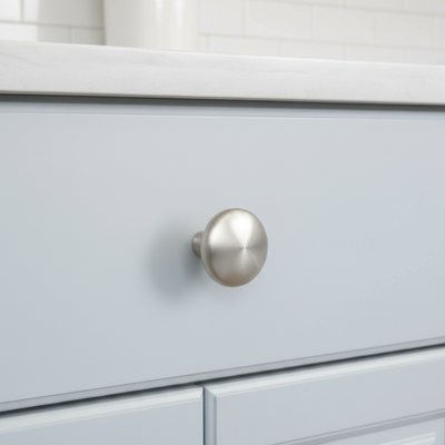 Close-up of a satin nickel round cabinet knob on a white drawer