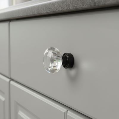 Clear glass cabinet knob on a gray drawer with a black base.