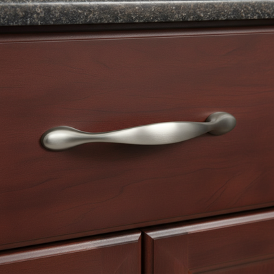 Close-up of a silver cabinet handle on a wooden drawer with a granite countertop.
