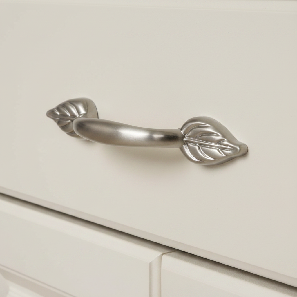 satin nickel cabinet pull with a leaf design on a white cream cabinet drawer 