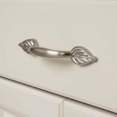 satin nickel cabinet pull with a leaf design on a white cream cabinet drawer 