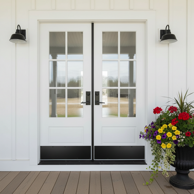 Black kickplates on White double French door entryway with black trim, black door handles, black wall sconces, and a potted flower arrangement on a wooden deck.