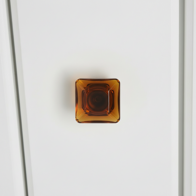Amber-colored square glass cabinet knob installed on a white cabinet drawer 
