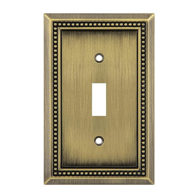 Antique brass single toggle switch plate with decorative border on a white background