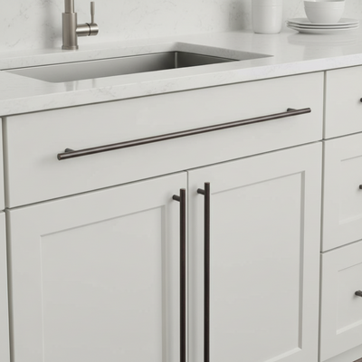 White kitchen cabinets with black handles and a stainless steel sink.