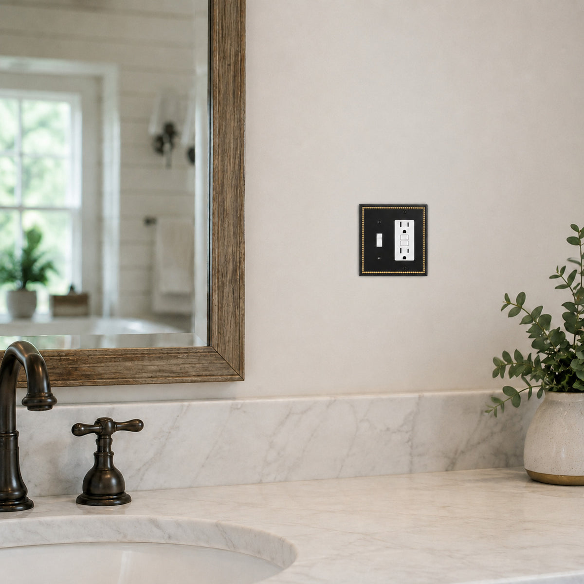 A modern black double outlet cover plate with gold trim mounted on a bathroom wall above a marble countertop and sink.