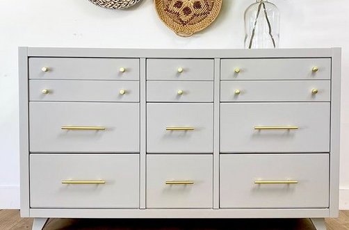 Cosmas 305-030BB Brushed Brass Euro Style Bar Pull on a white cabinet with round knobs