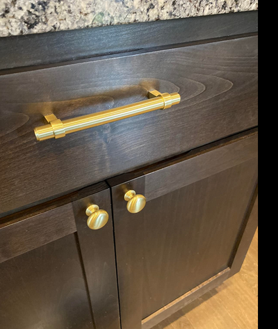 The 161-4BB and the Cosmas 4950BB Brushed Brass Cabinet Knob on a dark wood cabinet drawer and cabinet door