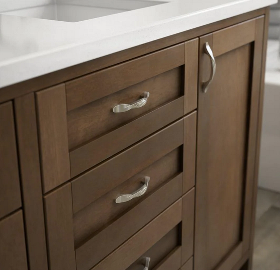 Cosmas 9009SN cabinet pull on a brown bathroom vanity with three drawers and one cabinet door. The cabinet vanity has a white marble countertop and satin nickel twist knobs are on the drawers and  cabinet door. 