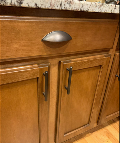 Cosmas 9236ORB Oil Rubbed Bronze Cabinet Cup Pull on a wood cabinet with a marble countertop and oil rubbed bronze bar pulls. 