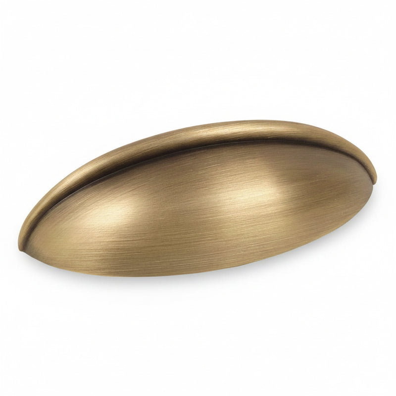 Oblong drawer pull in brushed antique brass finish with two and a half inch hole spacing. Cosmas 1399BAB cup pull in brushed antique brass. 