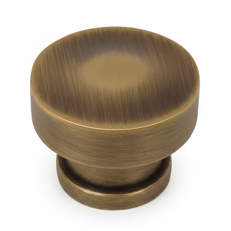 Round rigid cabinet knob in brushed antique brass finish with one and a quarter inch diameter
