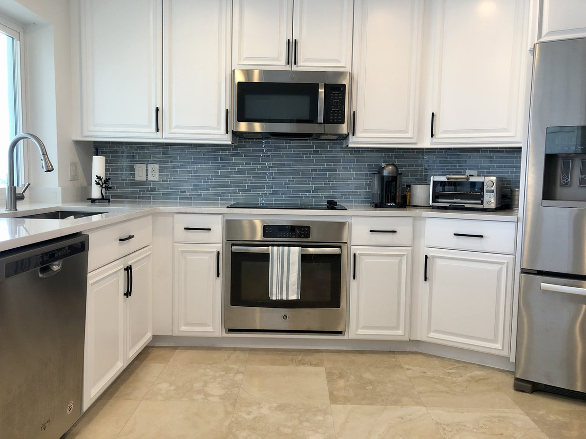White kitchen with black Cosmas 7-1/2" pulls, staineless steel appliances and blue backsplash